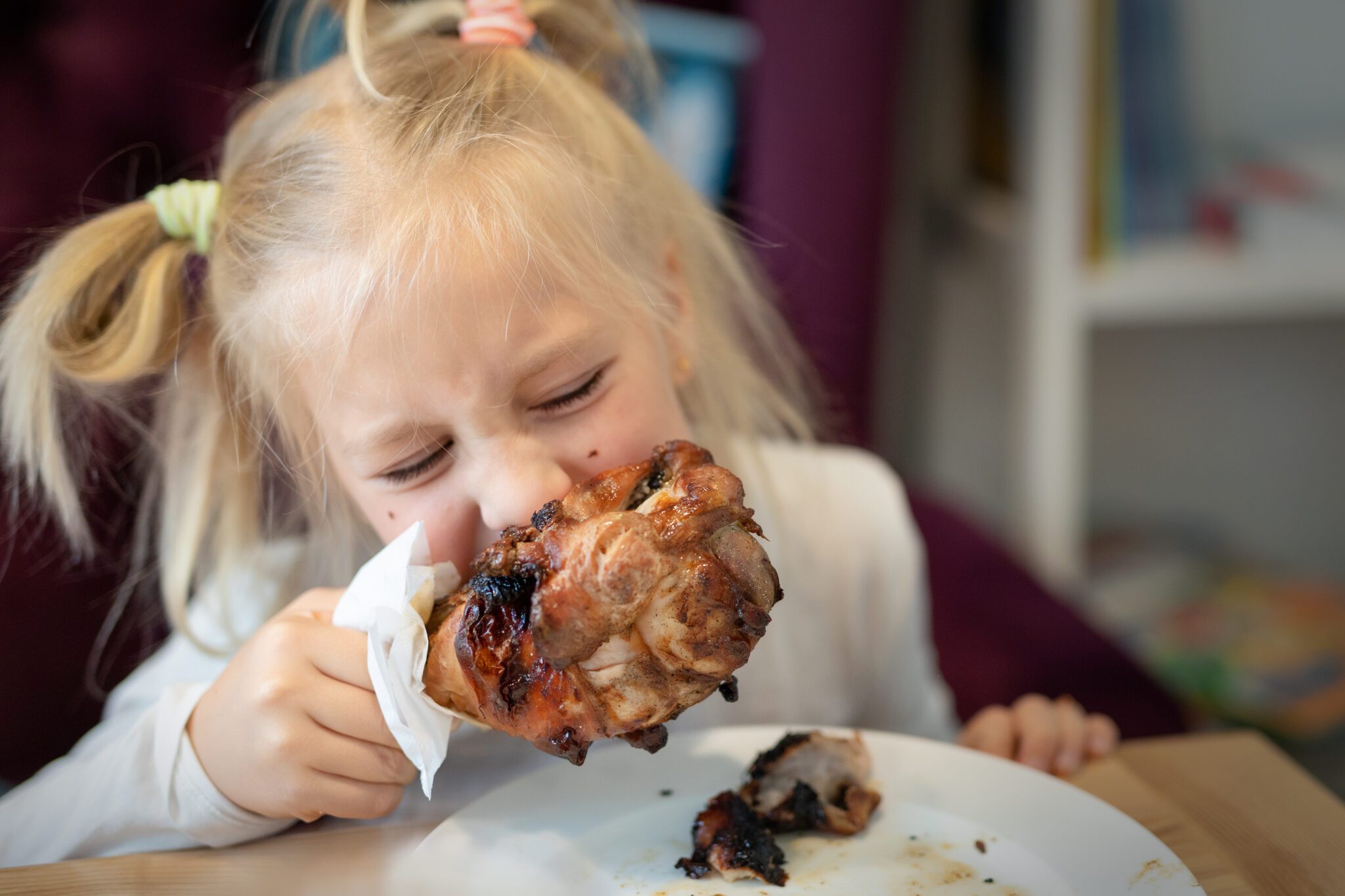 cute adorable caucasian blond little girl portrait enjoy eating roasted turkey shank at dinner at restaurant or cafe indoors. happy small hungry kid biting fat big meat. children healthy diet